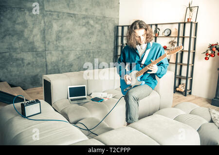 Künstlerische junger Mann aktiv spielen auf der Gitarre in der Mitte der Zimmer Stockfoto