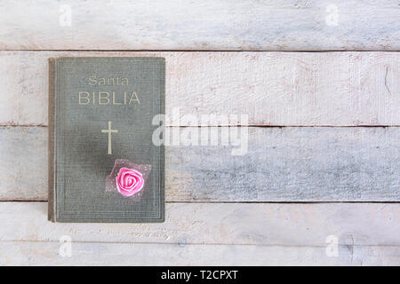 Heilige Bibel mit dem Wort biblia in spanischer Sprache mit einer Rose Blume Dekoration auf einem Holztisch. Ansicht von oben und der leere Raum für Editor's Text. Stockfoto