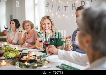 Eine große Familie an einem Tisch sitzen auf einem Indoor Party, klirren Gläser mit Rotwein. Stockfoto