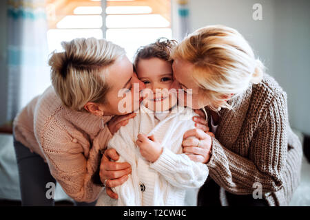 Ein Porträt von glücklichen kleinen Mädchen mit Mutter und Großmutter zu Hause, küssen. Stockfoto