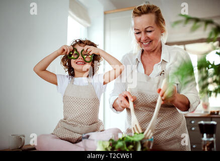 Ein Porträt von glücklichen kleinen Mädchen mit Großmutter Vorbereitung Salat zu Hause, Spaß zu haben. Stockfoto