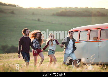 Eine Gruppe junger Freunde vor der retro Minivan auf einem Roadtrip durch die Landschaft läuft. Stockfoto