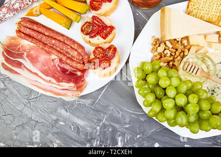 Italienische Antipasti Wein Snacks. Catering Plattenteller mit Antipasti, Salami, Käse, Weintrauben, Prosciutto, Brushettas auf grunge grauen Hintergrund. Italienisch Stockfoto