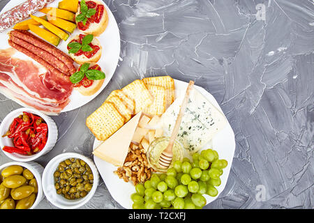 Italienische Antipasti Wein Snacks. Catering Plattenteller mit Antipasti, Salami, Käse, Weintrauben, Prosciutto, Brushettas auf grunge grauen Hintergrund. Italienisch Stockfoto