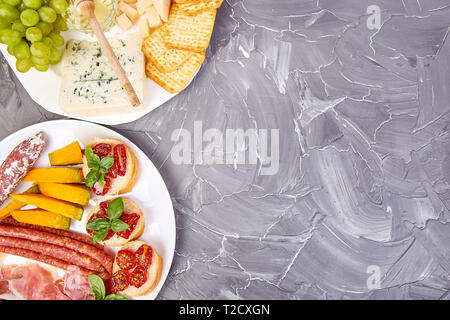 Italienische Antipasti Wein Snacks. Catering Plattenteller mit Antipasti, Salami, Käse, Weintrauben, Prosciutto, Brushettas auf grunge grauen Hintergrund. Italienisch Stockfoto