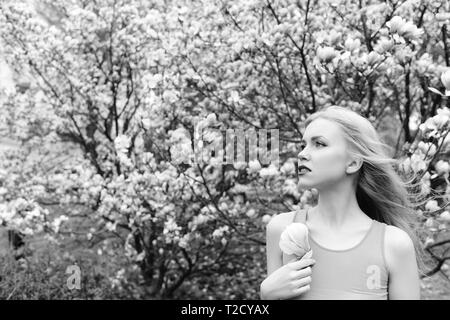 Feder. hübsches Mädchen mit blondem Haar und roten Lippen halten Magnolienblüte an blühenden Baum im Frühling Garten im Freien auf natürlichen Hintergrund Stockfoto