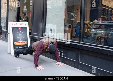 Ein unbekannter Mann hat pushups außerhalb eines Restaurants auf der East 12th Street am Broadway in Greenwich Village, Manhattan, New York City. Stockfoto