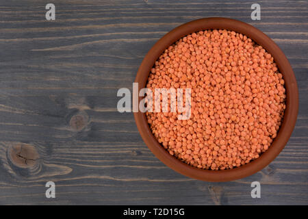 Rote Linsen in Ton Platte auf hölzernen Tisch Hintergrund Stockfoto