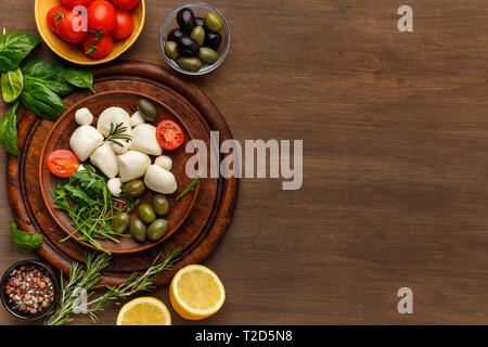 Mozzarella, Oliven, Gewürze, frische Kräuter und Gemüse auf Holz- Hintergrund, Ansicht von oben, kopieren. Italienische Küche Konzept Stockfoto