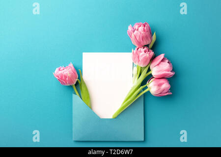 Blumenstrauß aus rosa Tulpen in türkis Umschlag auf Türkisfarbenem Hintergrund. Mockup mit weißen Karte. Flach, Ansicht von oben. Stockfoto