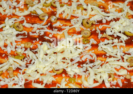 Hausgemachte Pizza gelben Käse und Oliven sind auf die Tomatensauce platziert Stockfoto
