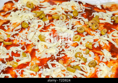 Hausgemachte Pizza gelben Käse und Oliven sind auf die Tomatensauce platziert Stockfoto