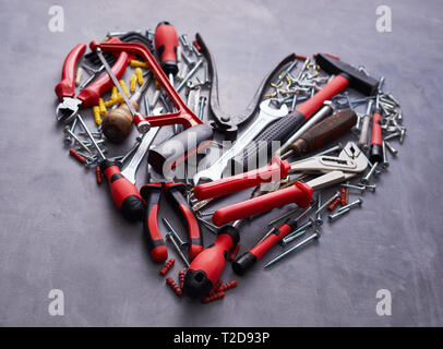Herz förmige Anordnung der sortierten rot Handwerkzeuge für die Holzbearbeitung auf eine strukturierte grauer Hintergrund in der Nähe zu sehen. Stockfoto