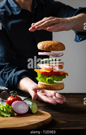 Levitation Burger zwischen den Händen vor einem dunklen Hintergrund. Stockfoto