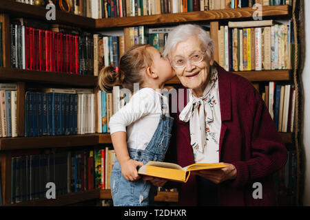 Glückliche Momente mit ihrer Urgroßmutter, ältere Dame viel Zeit mit ihrem großen Enkelin. Portrait vor einem Bücherregal, ein Buch, das ich Stockfoto