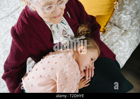 Glückliche Momente mit ihrer Urgroßmutter, ältere Dame viel Zeit mit ihrem großen Enkelin. Restless freche kleine Mädchen ein Nickerchen auf dem gre Stockfoto