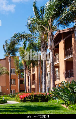 Resort Condominium mit grünen Palmen, grünes Gras und rot blühenden Büschen unter strahlend blauen Himmel. Terrassen, Balkone und Terrassen. Stockfoto