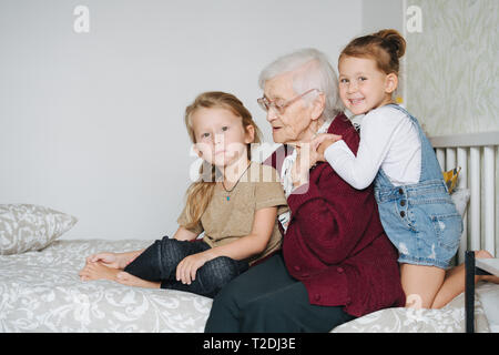 Glückliche Momente mit ihrer Urgroßmutter, ältere Dame viel Zeit durch ihre kleine große Enkelkinder umgeben. Portrait sitzen zusammen auf einem Bett in Stockfoto