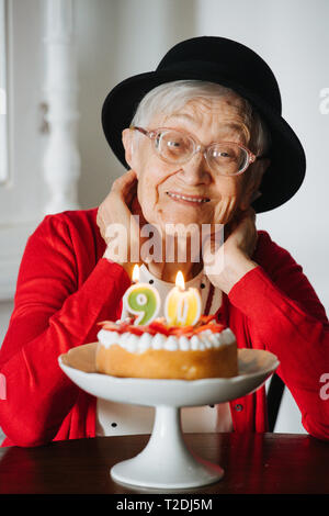 Senior glücklich gut in Schwarz mini-hut grau behaarte Frau ihren 90. Geburtstag zu Hause feiert gekleidet. Stockfoto