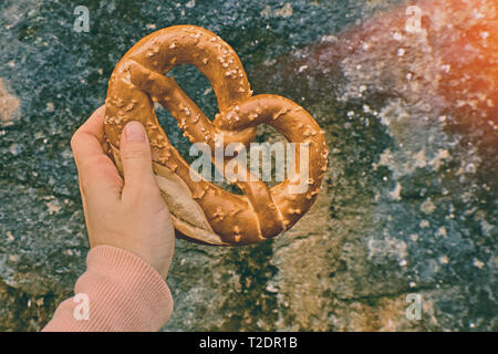 Junge Mädchen oder eine junge Frau hält einen traditionellen deutschen Brezel mit Alpen Berg Felsen im Hintergrund. Stockfoto