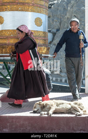 Eine buddhistische Mann und Frau mit Gebet und Gebet Perlen in der Hand, um ein riesiges gold Gebetsmühle in Leh-Ladakh. Indien Stockfoto