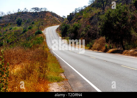 Gepflasterte Straße, Kurvt durch Mountain Pass mit braunen trockenes Gras und grüne Büsche auf der Straße. Stockfoto