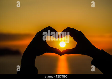 Ein Herz, das mit Händen gemacht mit der Sonne im Inneren bei Sonnenaufgang und Sonnenuntergang, Sonne Stockfoto