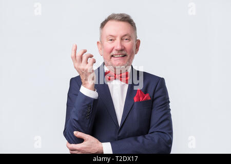 Freundlich älterer Mann im blauen Anzug duscussing Frage mit ihnen mit offenen Händen Geste und lächelte Kamera Stockfoto
