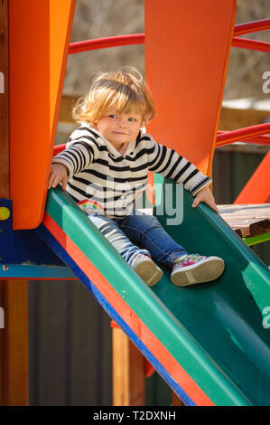 Süße kleine blonde Kleinkind Mädchen Rutschen für die Kinder am Spielplatz schieben Stockfoto