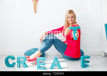 Junge stilvoll Kreative blonde Frau mit Buchstaben T auf dem Boden Stockfoto