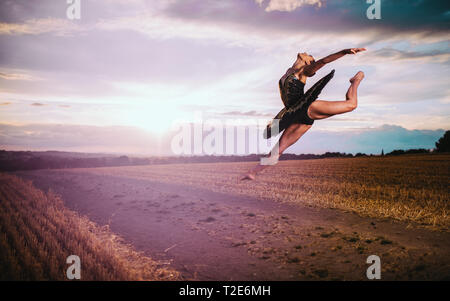 Balletttänzerin, die durch die Luft springt und im Hintergrund die Sonne untergeht. Stockfoto