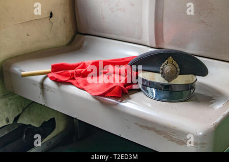 SAMUT SONGKHRAM, THAILAND, Okt 06 2018, die Kappe der Thailändischen Eisenbahner mit der roten Flagge auf die veralteten Sitz im alten Wagen. Stockfoto