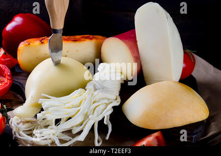 Sortierte hausgemachten Käse in verschiedenen Formen und Größen auf dem hölzernen Hintergrund, suluguni, Zopf, Cacocavallo mit Tomaten und Kräutern Stockfoto