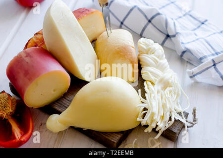 Sortierte hausgemachten Käse in verschiedenen Formen und Größen auf dem hölzernen Hintergrund, suluguni, Zopf, Cacocavallo mit Tomaten und Kräutern Stockfoto