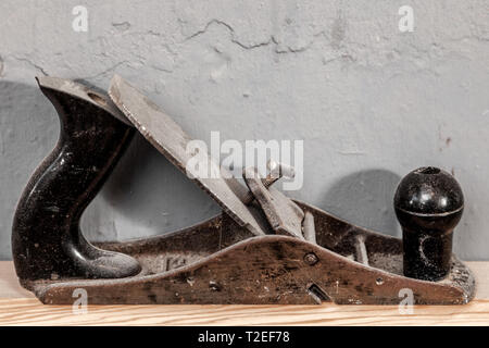 Close-up Black Metal Hobel- und Kunststoff für die Verarbeitung von Holz steht auf einem Holztisch vor dem Hintergrund einer grauen Wand Stockfoto