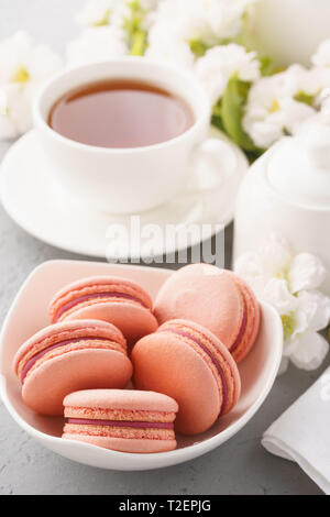 Rosa französische Macarons mit Beeren füllen und Kaffee zum Dessert. Blumen im Hintergrund. Stockfoto