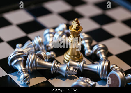 Satz silber Schachfiguren platziert an Bord rund um Golden King nach der Niederlage Stockfoto