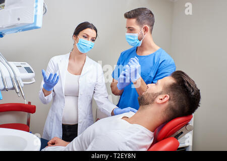 Ein stattlicher Zahnarzt und eine junge Assistentin Beratung mit dem Patienten im Zahnarztstuhl. Stockfoto