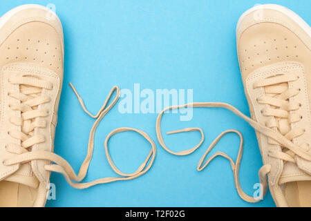 Neue Frauen Sportschuhe mit Schnürsenkeln aus Yoga Text. Flach auf blauem Hintergrund. Stockfoto