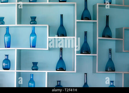 Retro Style Blau Glas Flaschen in einer schönen Anordnung in den Regalen zu einem hellblauen Wand befestigt. Stockfoto