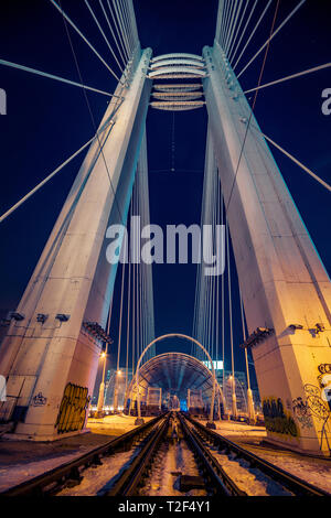 Night Shot von zwei Schienen der Straßenbahn für die öffentlichen Verkehrsmittel, die über eine moderne Brücke mit hohen Säulen im Winter in Bukarest Rumänien verwendet Stockfoto