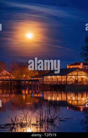 Schöne Nacht Szene auf dem See mit einem hellen Mond auf dem bewölkten Himmel mit beleuchteten Gebäuden auf dem See Stockfoto