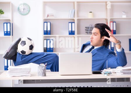 Junge gut aussehender Geschäftsmann mit Fußball im Büro Stockfoto