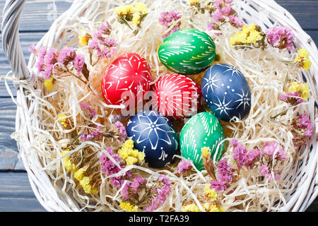 Von Hand bemalt, verschiedene Farben Ostereier im Nest und Blumen auf grau Holztisch mit Platz für Text Stockfoto