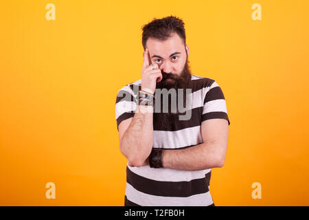 Bärtige hipster jungen Mann denken über gelben Hintergrund im Studio Foto Stockfoto