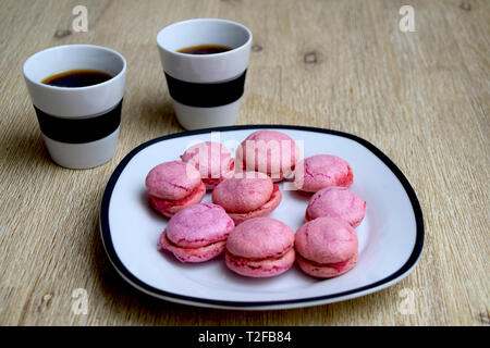 Tasse Kaffee und Rosa französische Macarons mit Himbeer-Füllung auf einer Platte Stockfoto