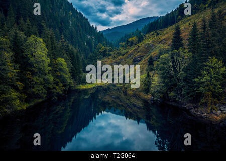 Ein schöner See tief in den Bergen von einem Wald am Anfang Herbst umgeben an einem bewölkten Abend vor Dunkelheit und einige Reflexionen entfernt Stockfoto