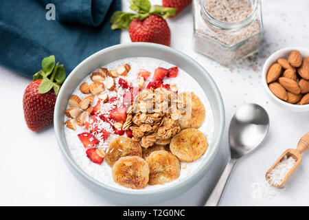 Smoothy Schüssel mit Banane, Erdbeere, Müsli, Nüsse auf weißer Tisch. Detailansicht. Konzept der gesunde vegetarische Diät, Gewichtsverlust, ausgewogene Ernährung Stockfoto