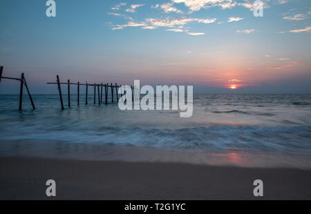 Alte kaputte Pier am Strand den Sonnenuntergang im Hintergrund. Stockfoto