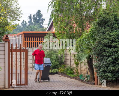 Johannesburg, Südafrika - Unbekannter ältere Hausbesitzer verschiebt eine Mülltonne auf dem Pflaster für die wöchentliche kommunale Müllabfuhr Stockfoto